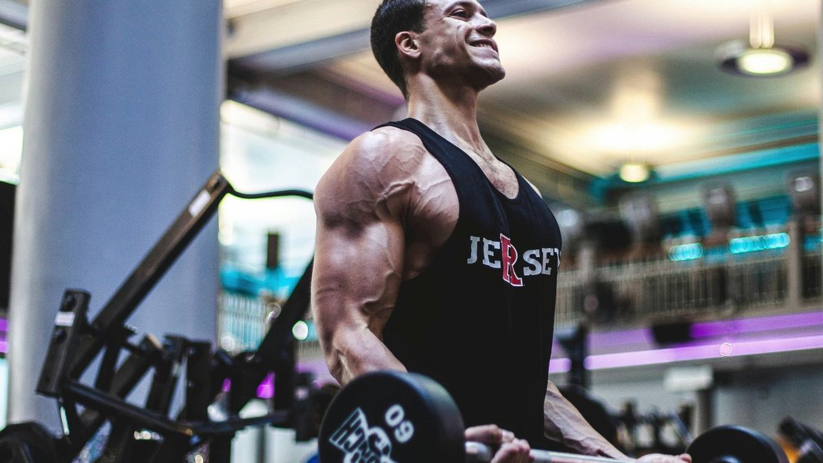 Man doing biceps curls with a fixed-weight curl bar in a gym